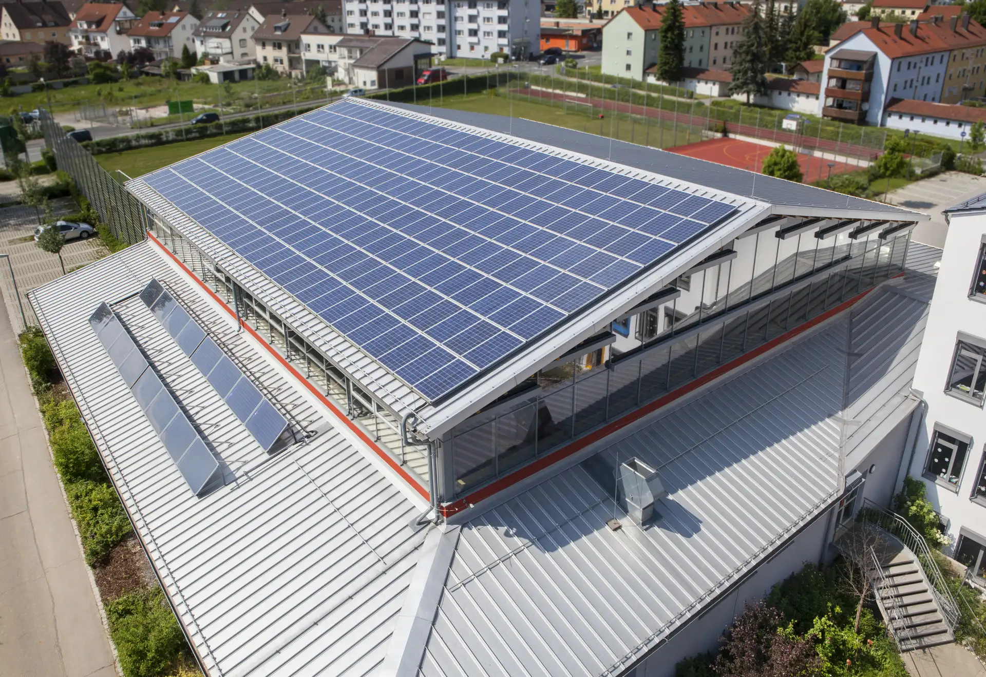 Großflächige Solaranlage auf dem Dach der Sporthalle der Pestalozzi Grundschule in Sulzbach-Rosenberg mit Blick auf das Schulgebäude und umliegende Wohnhäuser