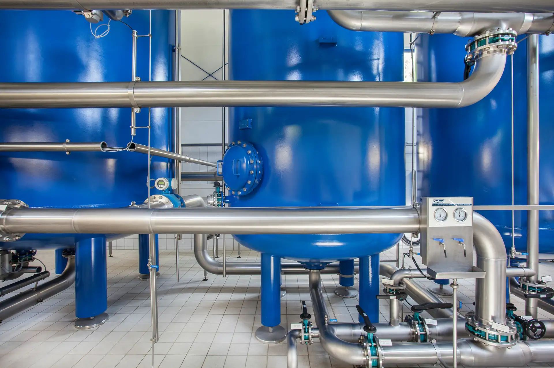 Blick in eine moderne Wasseraufbereitungsanlage mit großen blauen Druckbehältern und Edelstahlrohrsystemen