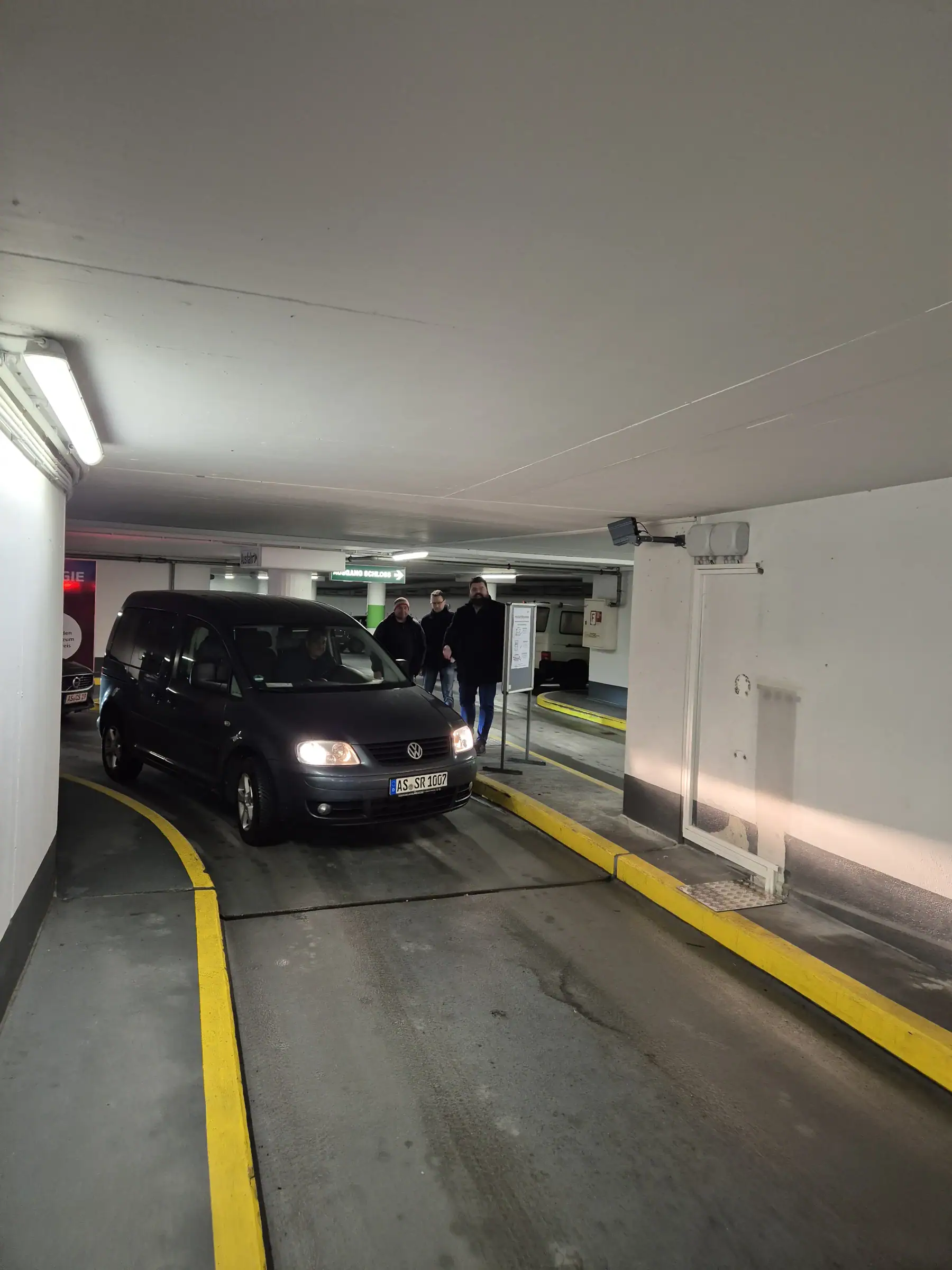 Ein Mitarbeiter fährt mit einem schwarzen VW aus der Tiefgarage Sulzbach-Rosenberg. Im Hintergrund stehen Personen nahe der Ausfahrt. Die Schranke ist geöffnet, das Fahrzeug wird per Kennzeichenerkennung erfasst.